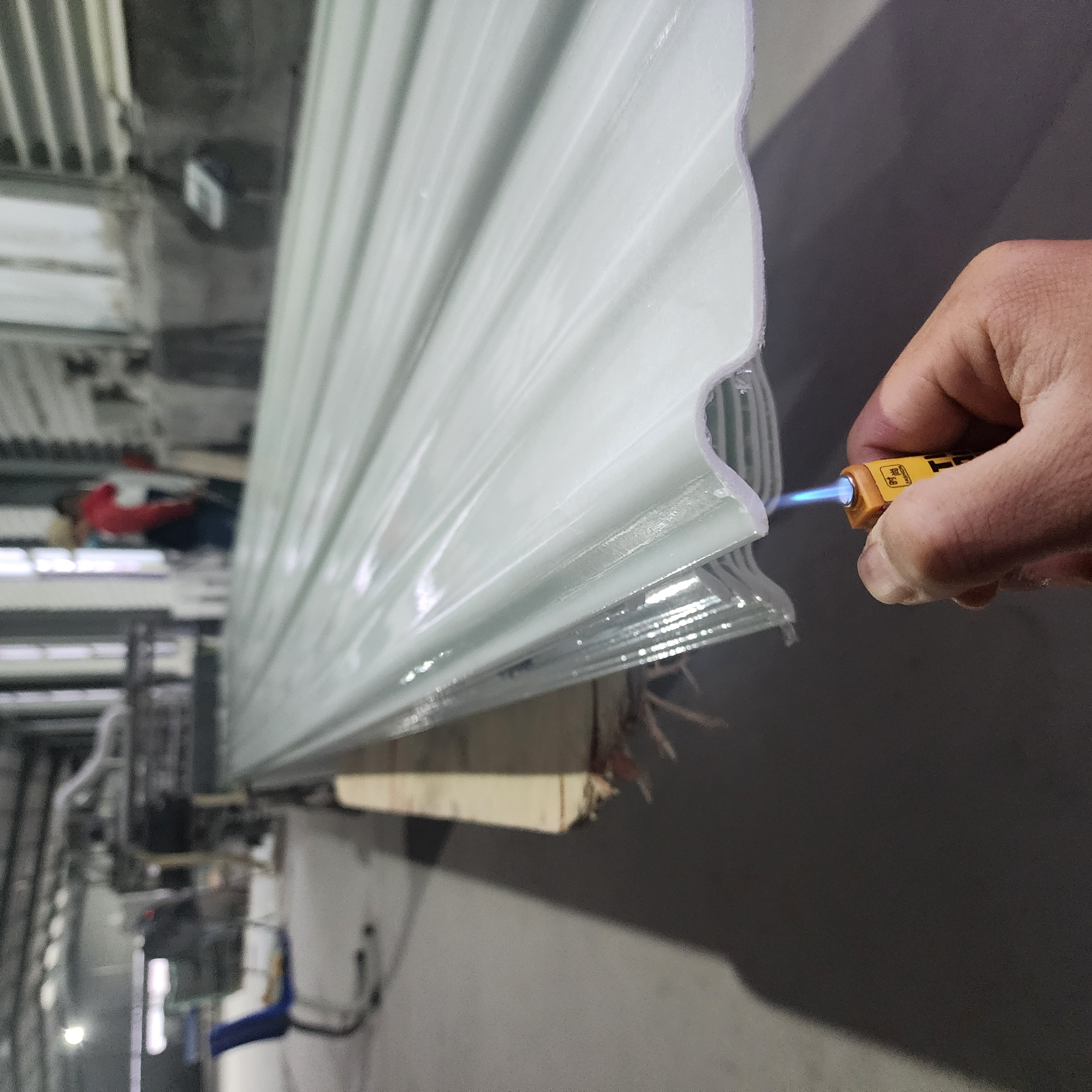 Flame-retardant FRP sheet test showing blue flame under sheet profile edge
